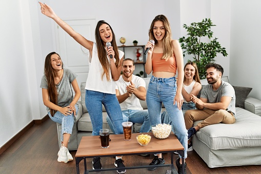 Group of young friends having party singing song using microphone at home.