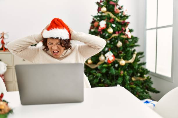 istock Middle age hispanic woman using laptop sitting by christmas tree suffering from headache desperate and stressed because pain and migraine. hands on head. 1333980135