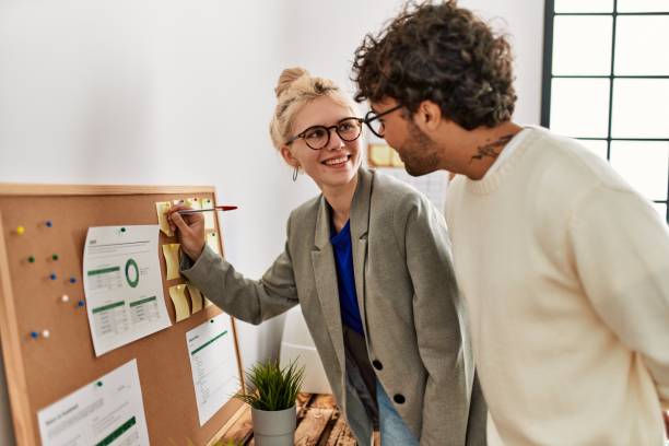 istock Two business workers smiling happy writing at corkboard reminder at the office. 1333981950
