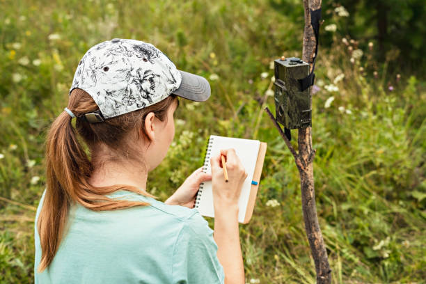 istock Young woman scientist zoologist writing down data from trap camera to notepad, observing wild animals in taiga forest, monitoring of rare and endangered animal species, ecology World Wildlife Day 1333982342