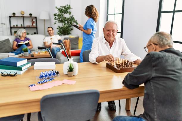 deux retraités souriant heureux de jouer aux échecs à la maison d’infirmière. - senior adult leisure games playing care photos et images de collection