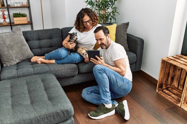 中年ヒスパニックカップルは幸せでタッチパッドを使用して微笑んでいます。自宅で犬とソファに座っています。 - husband wife couple senior adult ストックフォトと画像