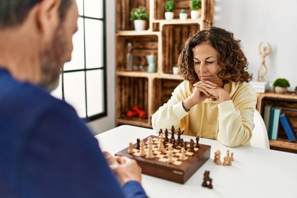 Middle age hispanic couple concentrated sitting on the table playing chess at home.