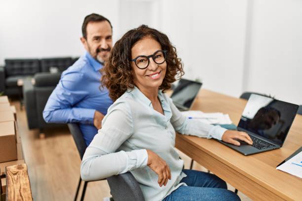 オフィスで働いて幸せそうに微笑む2人の中年のビジネスワーカー。 - happiness women senior adult two people ストックフォトと画像
