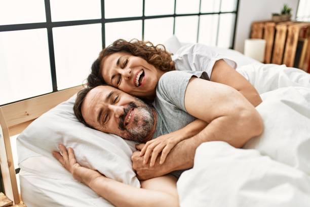 Middle age hispanic couple smiling happy and hugging lying on the bed at home. stock photo