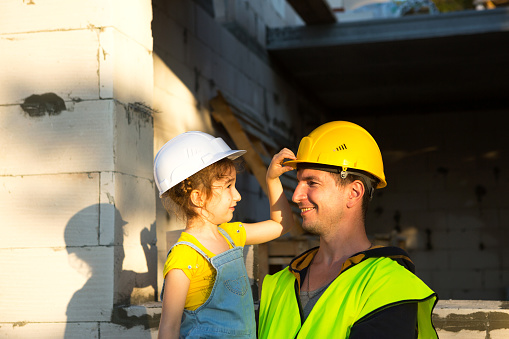 Dad and daughter are at construction site of their future home. The choice of the future profession of a builder is inherited by child. The expectation of moving, the dream of a house. Mortgage, loan