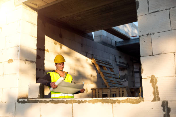 istock A construction engineer and designer in a yellow hardhat studies a drawing of a building on a construction site. A house made of porous concrete blocks, a worker in the process at the window and wall 1333984664