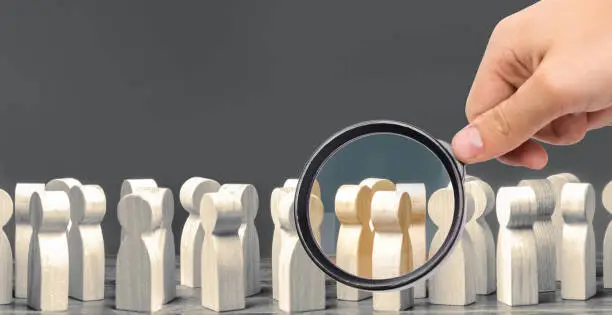 Photo of A magnifying glass looks at a crowd of wooden figures of people. society, demographic. group of citizens, rally, political movement or electorate. Customers and buyers, preferences of Population.