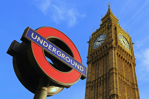 London, England, UK - Wide angle view looking up at Big Ben and a London Underground sign against a clear blue sky.
