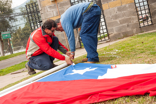 Santiago de Chile, Chile - September 1, 2019: A group of workers hoisting Chilean flag at the street in a cloudy winter day, some days before Chilean National Day, September 18th.