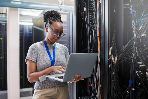 foto de una joven usando una computadora portátil en una sala de servidores - data center computer programmer women fotografías e imágenes de stock