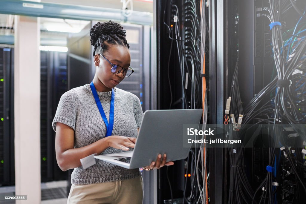 Shot of a young woman using a laptop in a server room Conducting repairs on a few parts Technology Stock Photo