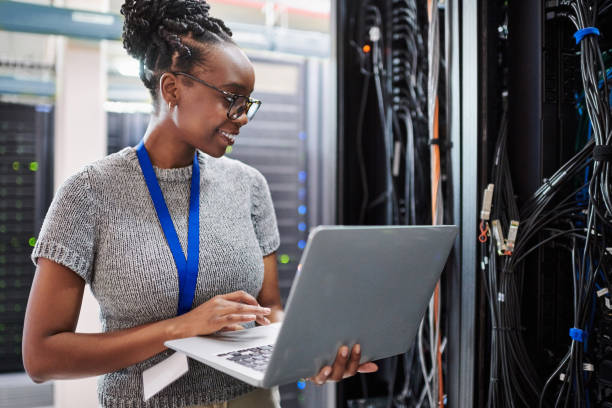 tiro de uma jovem usando um laptop em uma sala de servidor - data center computer programmer women - fotografias e filmes do acervo