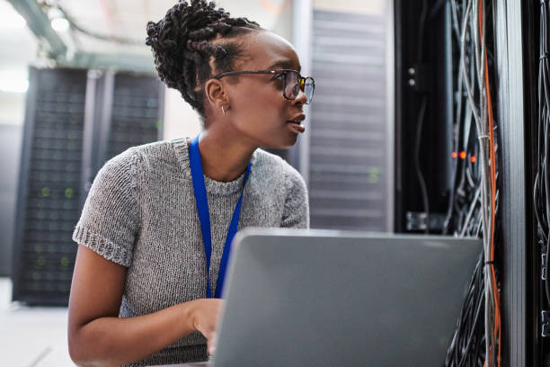 plan d’une jeune femme utilisant un ordinateur portable dans une salle de serveurs - telecommunications equipment technician repairing engineer photos et images de collection