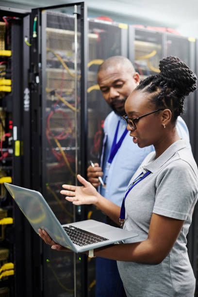 サーバールームのラップトップで一緒に働く2人の技術者のショット - telecommunications equipment technician repairing engineer ストックフォトと画像