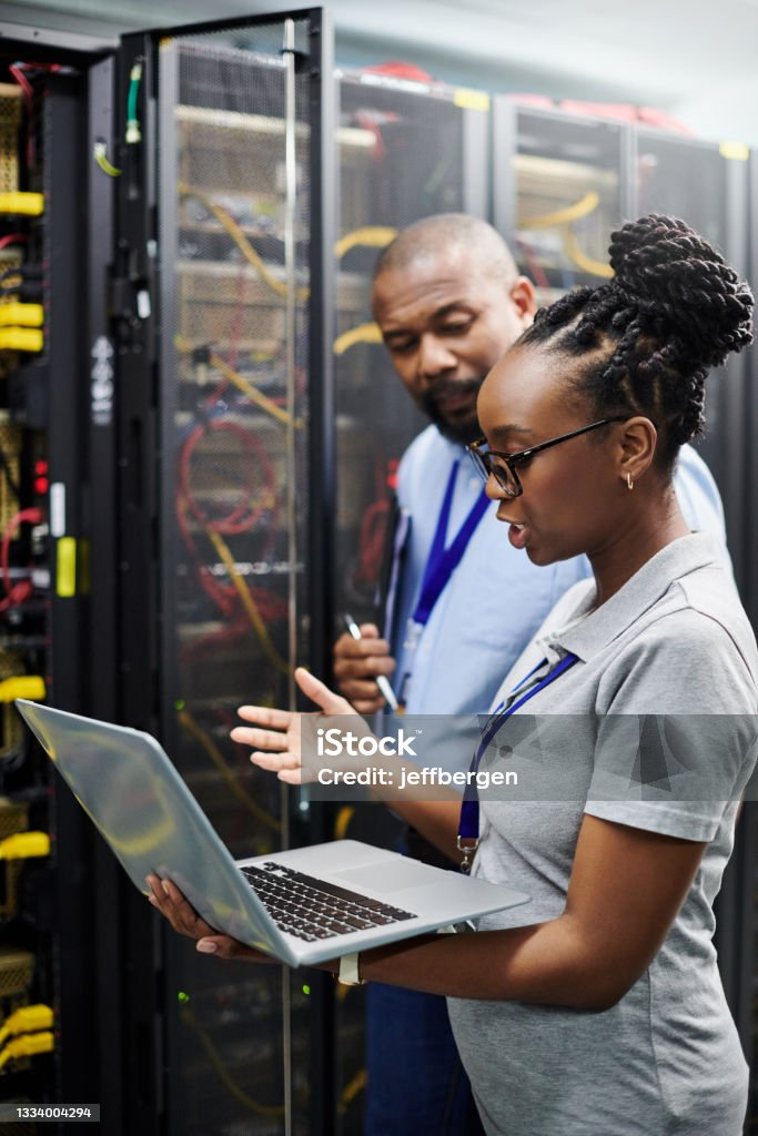 Shot of two technicians working together on a laptop in a server room Evaluating machine temperature levels for optimal performance Network Security Stock Photo