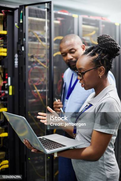 Shot Of Two Technicians Working Together On A Laptop In A Server Room Stock Photo - Download Image Now