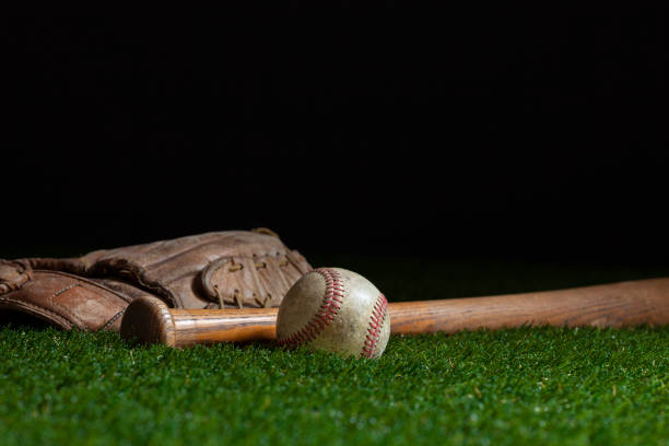 istock Old baseball bat and mitt low angle selective focus on grass field and dark background 1334004894