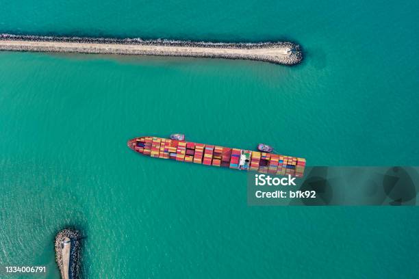 Aerial View Of Cargo Ship Approaching Port With Tugboat Stock Photo - Download Image Now