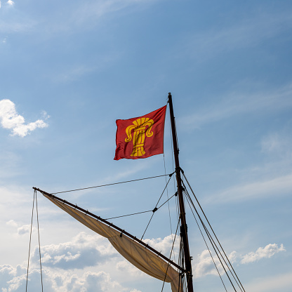 the flag of the Finnish city of Vaasa flying in a strong wind from the mast of an old sailboat under a blue sky