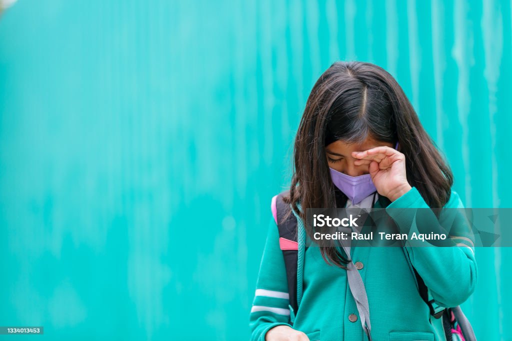 Mexican girl wearing uniform and face mask crying on the back to school Child Stock Photo