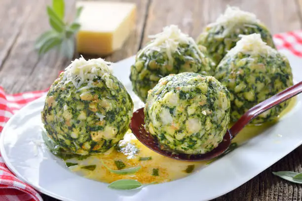 Homemade traditional South Tyrolean spinach dumplings made of white bread and fresh spinach leaves, served with melted sage butter and grated parmesan cheese on a white platter