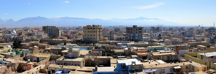 Mazar-i-Sharif, Balkh province, Afghanistan: city skyline - traditional adobe houses and modern buildings with the mountains in the background. Mazar-e-Sharif is the fourth largest city in Afghanistan, the name of the city means 'Tomb of the Exalted' and refers to the presumed burial place of Ali ibn Abi Talib, cousin and son-in-law of Muhammad, honored by Sunnis, Shiites and Alevis. Historically part of Bactria and the ancient region of Khorasan.
