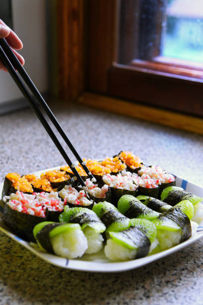 Close-up of different flavors of sushi on a plate, one hand using chopsticks to hold sushi, Japanese cuisine, depth of field