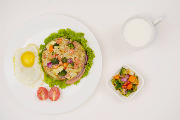 istock Close-up vegetable fried rice in white plate, fried egg, vegetable salad, milk, tomatoes, delicious nutritious lunch, top view 1334032981