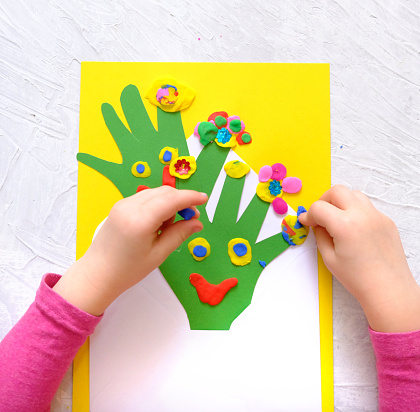 Little girl making homemade greeting card from envelope, paper own palms and decoration clay, plasticine as gift for Mothers day, Birthday or Valentines day . Arts  crafts concept.