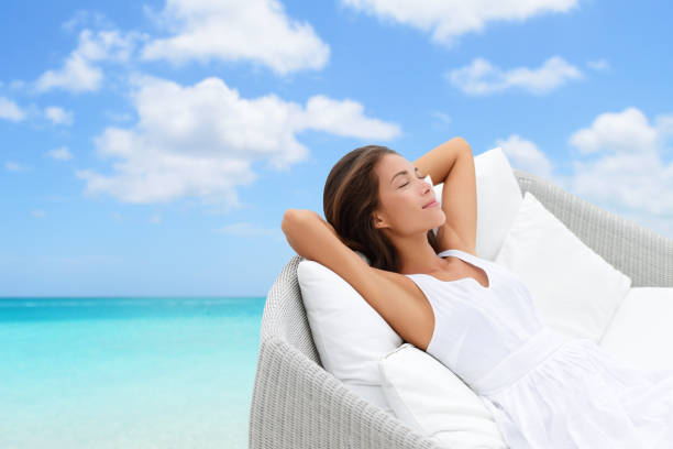 Back view of carefree woman with sun hat relaxing on a terrace and looking at sunset view above the sea. Copy space.