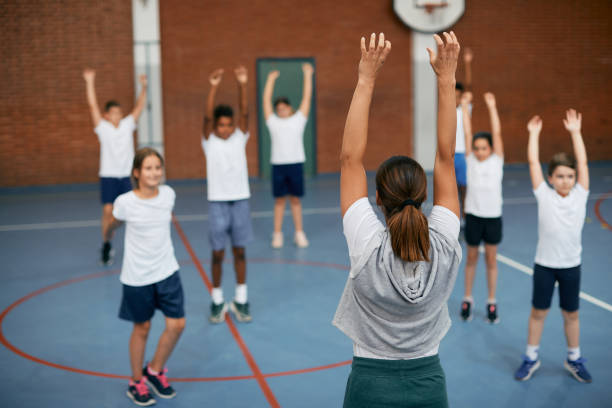 istock Rear view of coach and her students warming up during physical education at elementary school gym. 1334047462