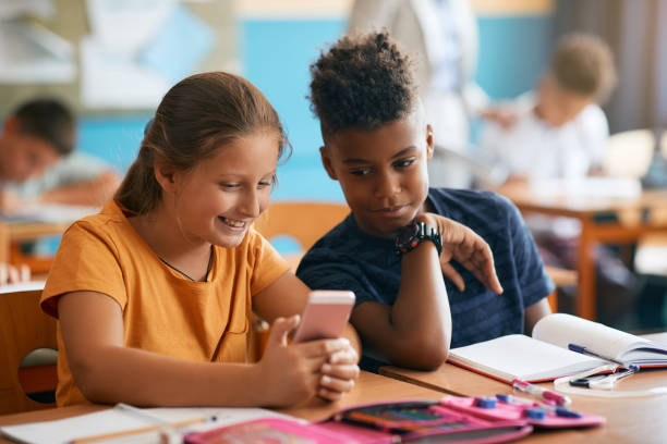 istock Happy classmates using cell phone in the classroom at elementary school. 1334049180