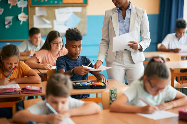 istock Black elementary student receiving exam paper from teacher during class at school. 1334049296