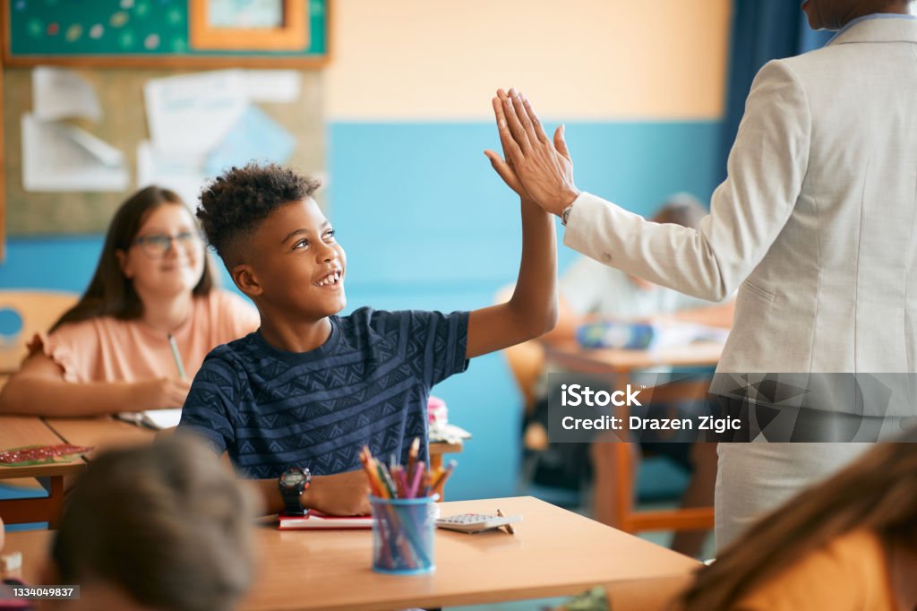 Glücklicher schwarzer Grundschüler und sein Lehrer, der während des Unterrichts in der Schule High Five gibt. - Lizenzfrei Lernender Stock-Foto