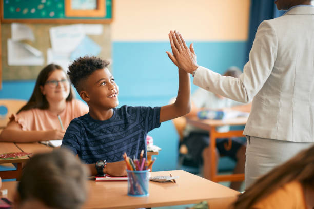 Happy black elementary student and his teacher giving high five during class at school. Happy African American schoolboy giving high-five to his teacher during  class in the classroom. pre adolescent child stock pictures, royalty-free photos & images