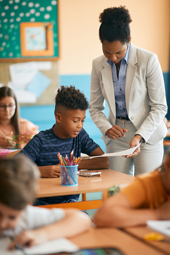 African American elementary student and his teacher analyzing test results during class at school.