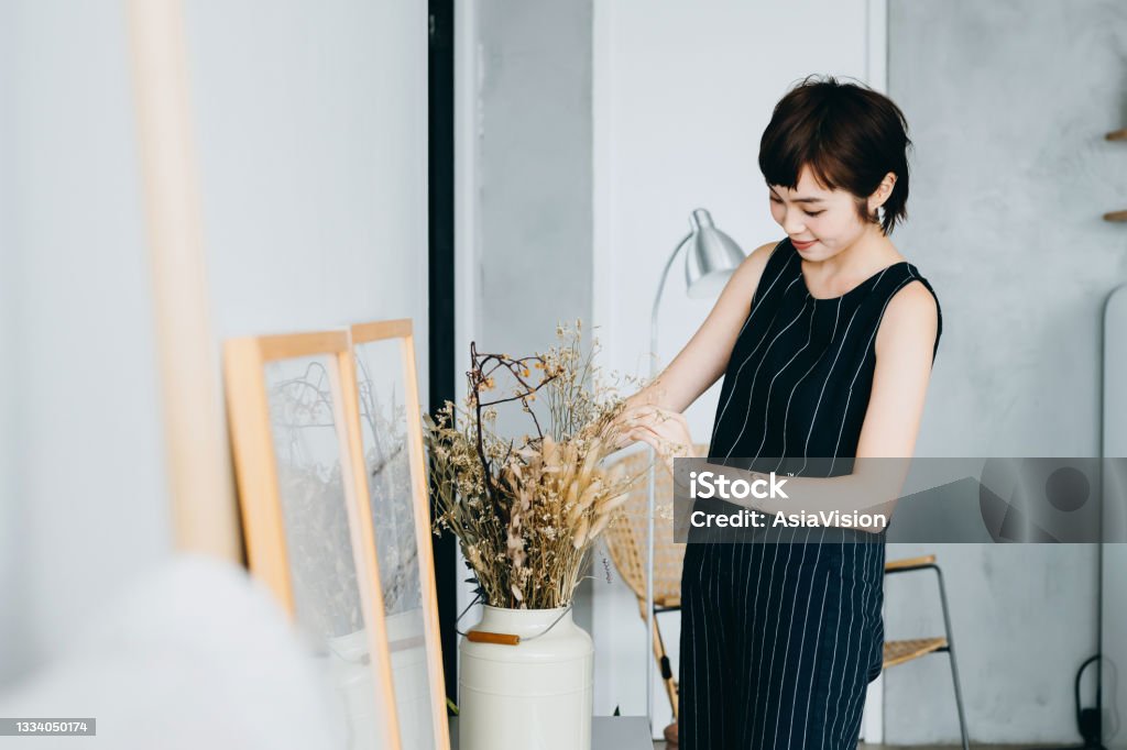 Young Asian woman decorating and arranging a vase with dried plants on cabinet in the living room at home Interior Designer Stock Photo