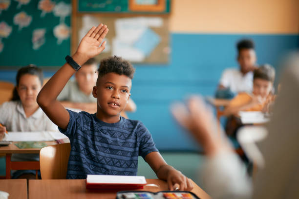 studente elementare nero alzando la mano per rispondere a una domanda durante le lezioni a scuola. - little boys pre adolescent child child education foto e immagini stock