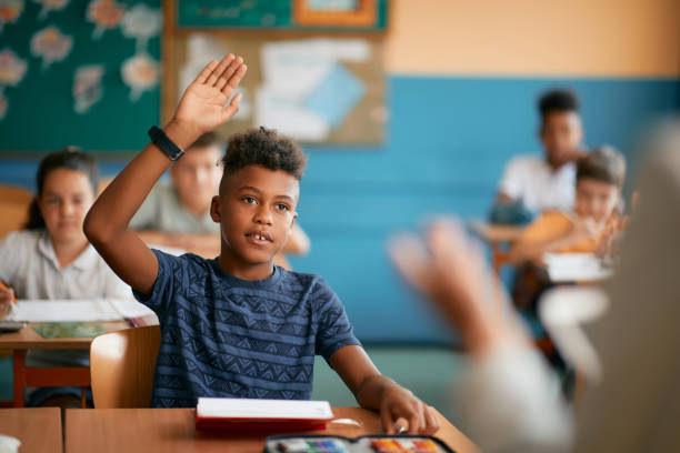 black elementary student raising his hand to answer a question during class at school. - 八歲到九歲 個照片及圖片檔