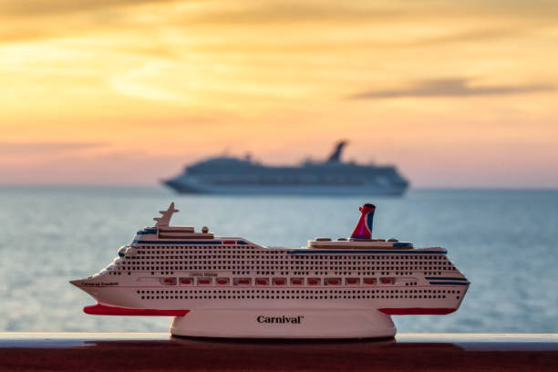 Gulf of Mexico - April 5, 2020: Small Carnival Freedom replica seating on a handrail. Blurred Carnival Valor sailing at orange sunset in the background.