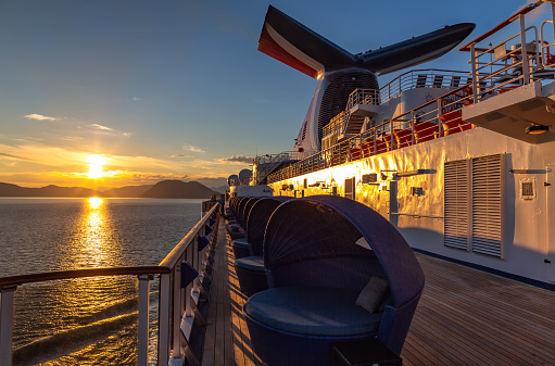 Alaska, USA - June 22 , 2018: Carnival Legend sailing at sunset in one of the Alaskan Fjords. Sun setting down and mountains in the background. View from the deck in the aft of the ship.