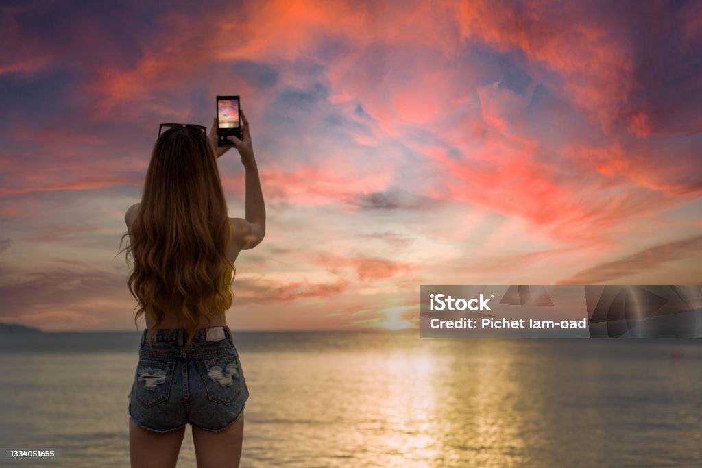 woman shootting photo of sunset at the beach by telephone Camera - Photographic Equipment Stock Photo