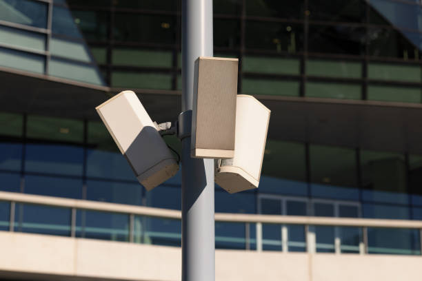 Outdoor speakers up a gray pole on a sunny day.