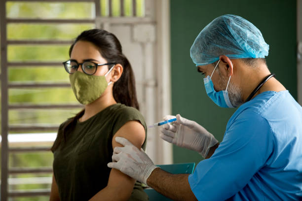 Doctor injecting vaccine to female patient Doctor wearing protective face mask and injecting vaccine into arm of patient antiviral drug stock pictures, royalty-free photos & images