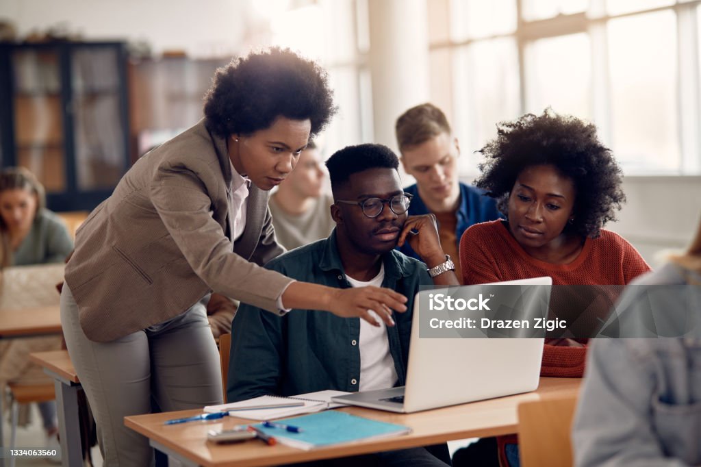 African Americans college students e-leaning with their teacher during a class. African American professor and her students using laptop during lecture in the classroom. University Student Stock Photo