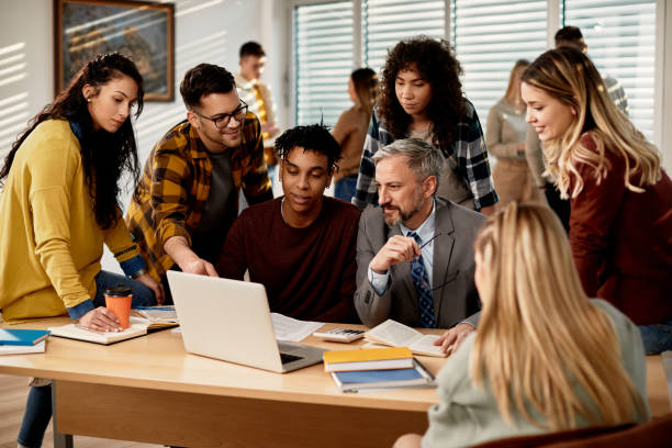 istock Mature teacher and group of his students using laptop at the university, 1334065509