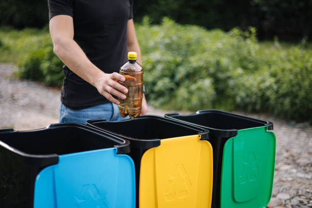 istock Close-up of human hand throwing empty plastic water bottle in recycling bin. Tree recycling bins outdoors 1334065685