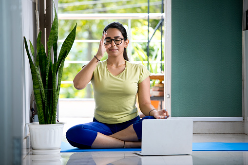 Young woman in yoga pose using laptop at home