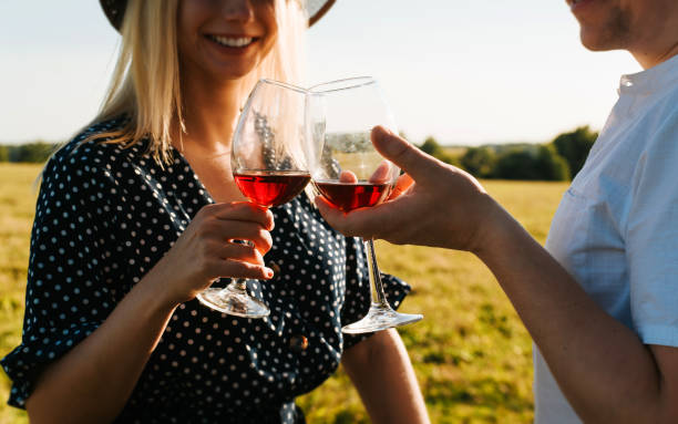 feliz encontro romântico do casal ao ar livre ao pôr do sol, close-up de taças com vinho tinto à luz do sol, os amantes de taças clink celebram em piquenique no campo. história de amor. foco seletivo em taças de vinho - women heterosexual couple love men - fotografias e filmes do acervo